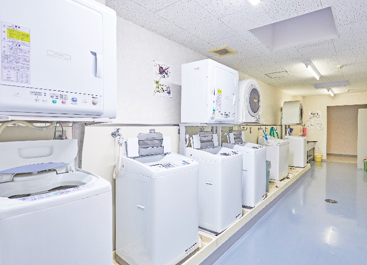 写真：女子寮の共用設備である洗濯場の様子。複数の洗濯機と乾燥機が設置されている。