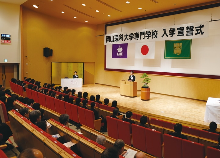 岡山理科大学専門学校入学宣誓式の様子　講堂にて学生が席に座り話を聴いている
